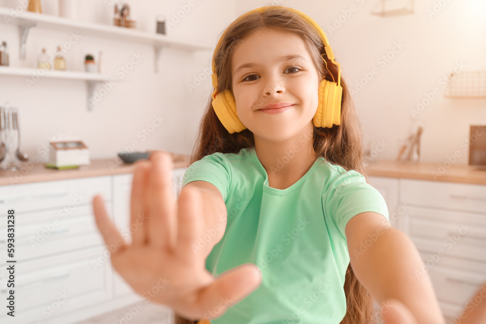 Happy little girl in wireless headphones dancing in kitchen Happy little girl in wireless headphones dancing in kitchen
