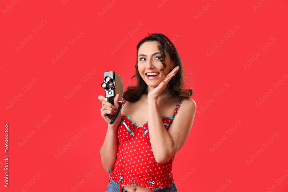 Obraz premium Young pin-up woman with retro video camera on red background