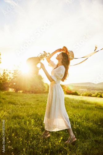 a woman in a white dress with a basket of daisies and a straw hat stands in a field during sunset in a light breeze