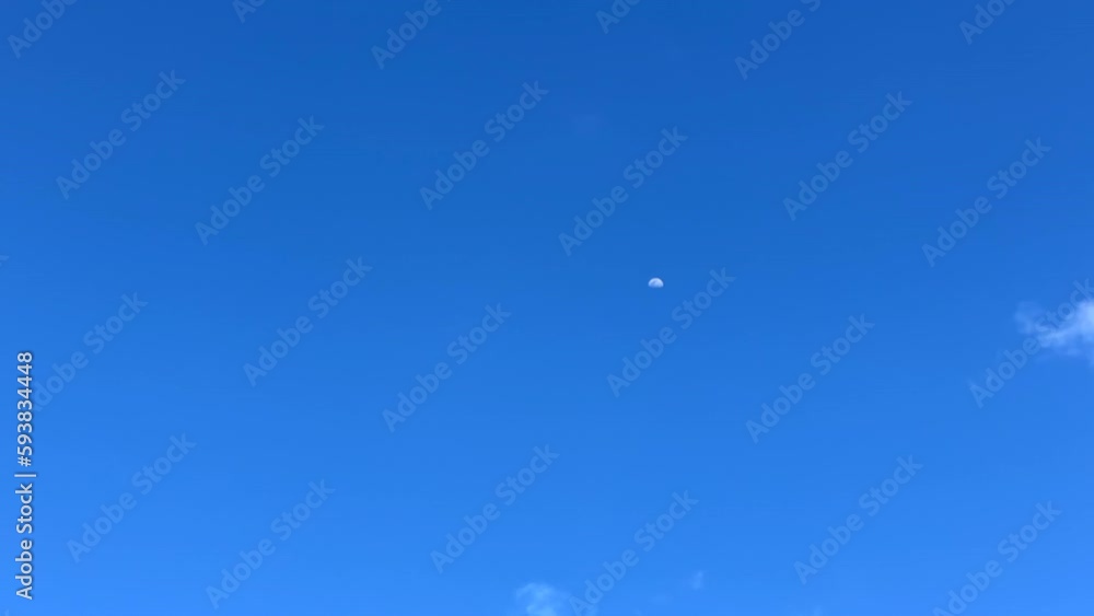 Time lapse, moon during day as clouds pass by in blue sky Time lapse, moon during day as clouds pass by in blue sky