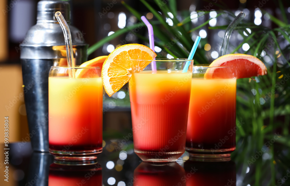 Glasses of delicious Tequila Sunrise and shaker on table Glasses of delicious Tequila Sunrise and shaker on table