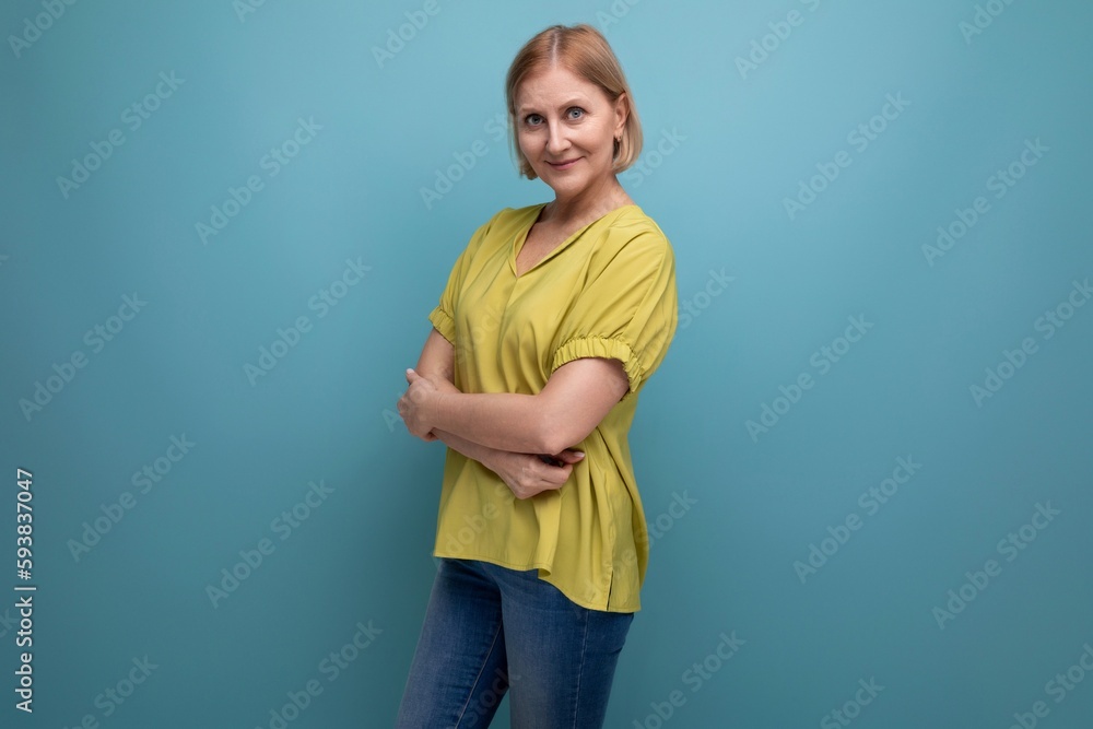 attractive 50s blonde woman in yellow t-shirt on blue background attractive 50s blonde woman in yellow t-shirt on blue background