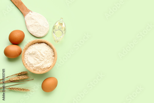 Composition with bowl of wheat flour, eggs, spoon and oil on green background