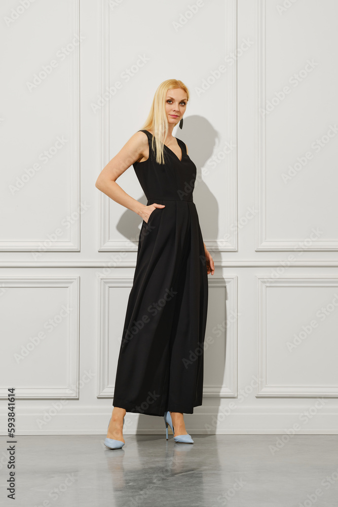 A blond businesswoman stands in a bright room, dressed fashionably in long black dress and wearing stilettos A blond businesswoman stands in a bright room, dressed fashionably in long black dress and wearing stilettos