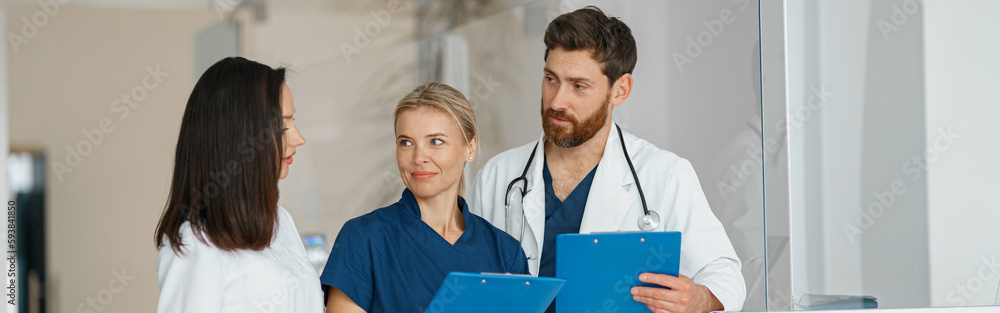 Group of doctor colleagues discussing patient diagnosis stand in clinic hall Group of doctor colleagues discussing patient diagnosis stand in clinic hall