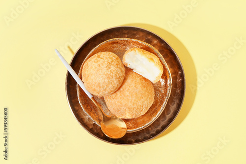 Plate with delicious choux pastry on yellow background