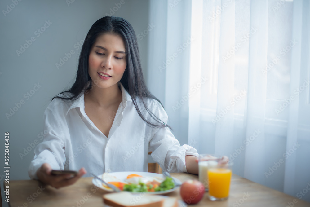 Beautiful asian woman enjoying good news on phone make her eat deliciously with smile on her face.