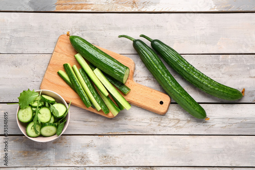 Bowl with fresh cut cucumber on light wooden background photo