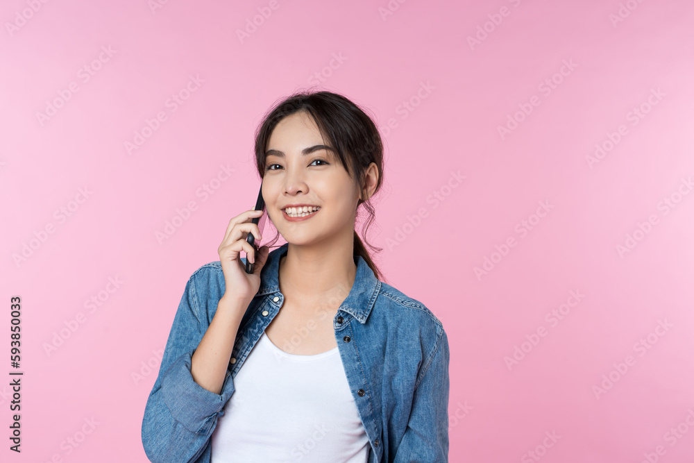 Yoing Asian woman talking on the phone holds cellphone making answering call on isolated pink background Yoing Asian woman talking on the phone holds cellphone making answering call on isolated pink background