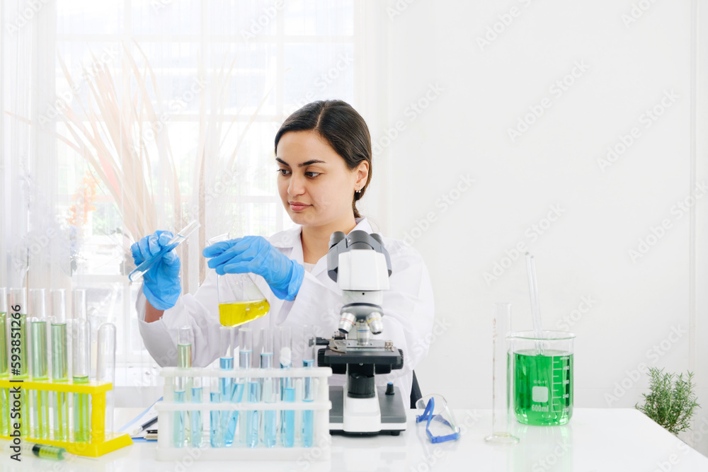 Middle East woman scientist researcher rinse liquid from a graduated cylinder to test tube for analysis of liquids in the lab. Scientist working with test tube and graduated cylinder. Middle East woman scientist researcher rinse liquid from a graduated cylinder to test tube for analysis of liquids in the lab. Scientist working with test tube and graduated cylinder.