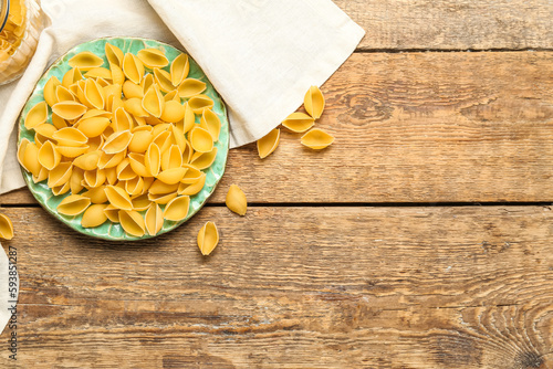 Plate with raw conchiglie pasta on wooden background photo