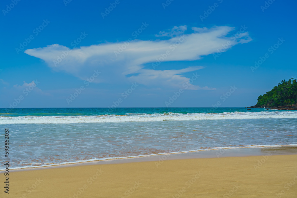 Sandy beach with low waves and clouds in the blue sky