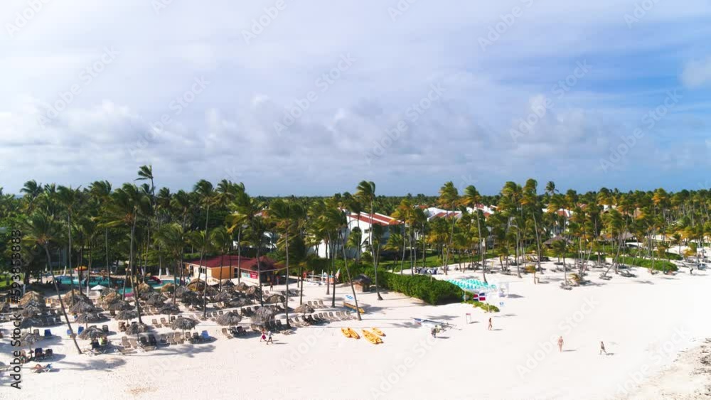 Tropical beach at tourist resort in Punta Cana Dominican Republic. Caribbean coastline with vacationers on a sunny summer day. Wide white sand paradise beach background with coconut trees. Tropical beach at tourist resort in Punta Cana Dominican Republic. Caribbean coastline with vacationers on a sunny summer day. Wide white sand paradise beach background with coconut trees.