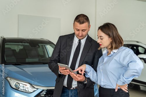 Beautiful client with salesman manager selling vehicle with tablet at car salon