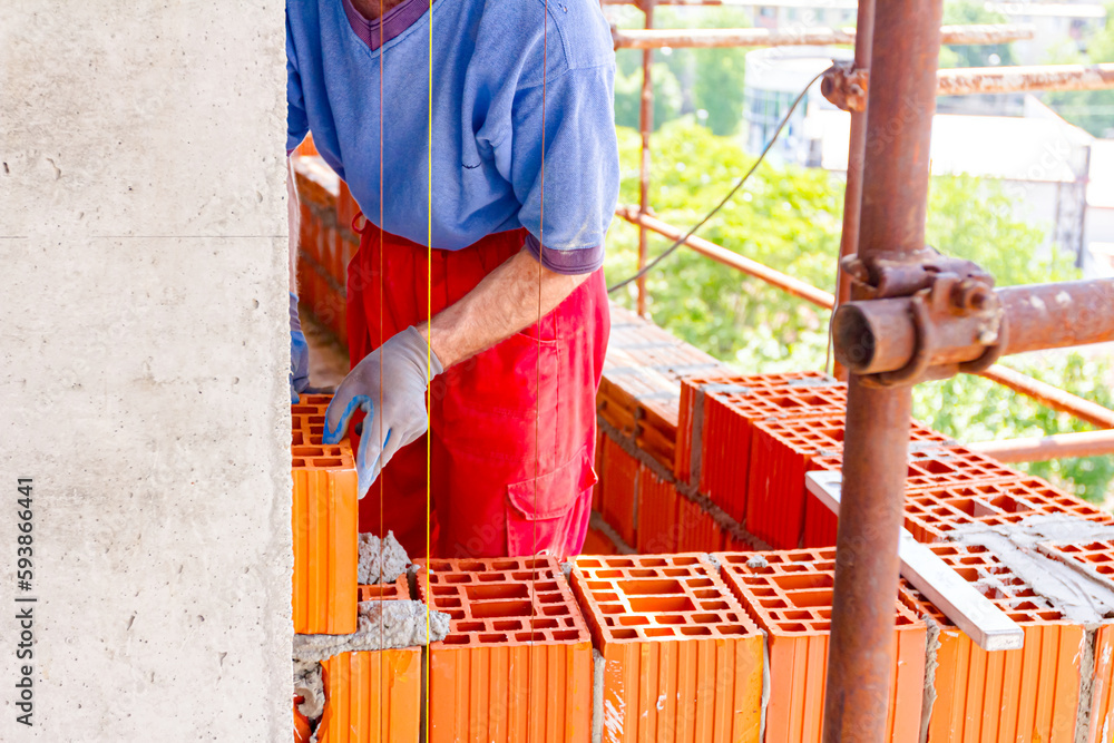 Worker is building wall with red blocks and mortar