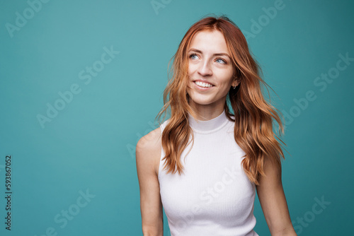 Joyful young excited woman wearing a white shirt. Happy and smiling cheerfully ginger hair woman portrait over mint studio background. Confident fit female. Happiness and lifestyle people.