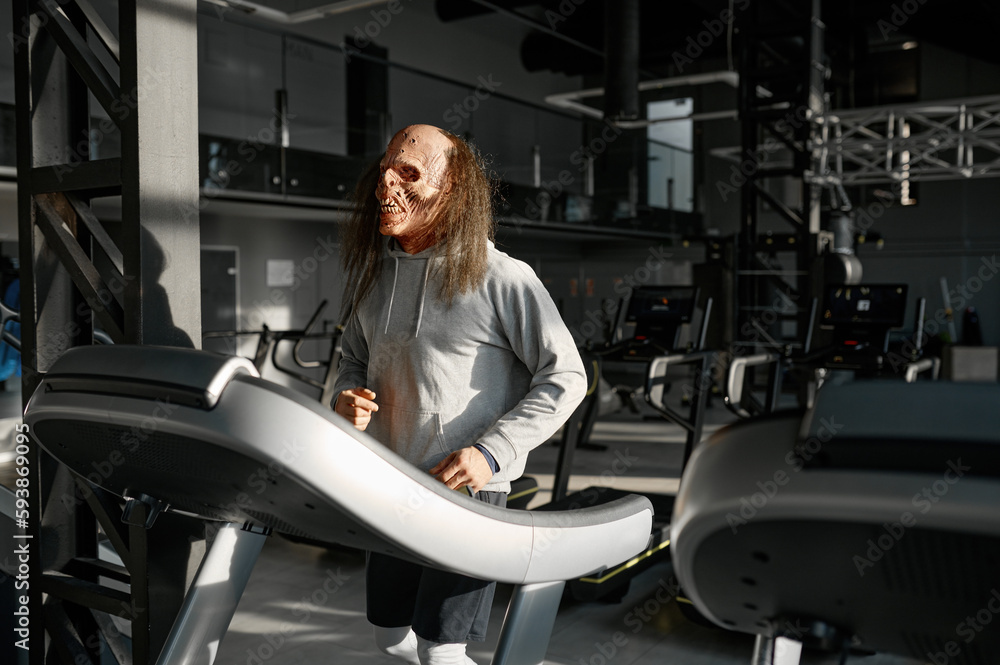 Zombie man with spooky face doing cardio workout on treadmill at gym Zombie man with spooky face doing cardio workout on treadmill at gym