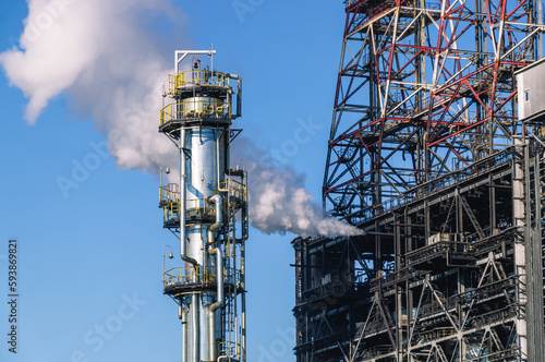 Oil refining plant. Technological equipment for the production of fuel components. White smoke escapes into the atmosphere from the production equipment at the refinery. White smoke and blue sky.