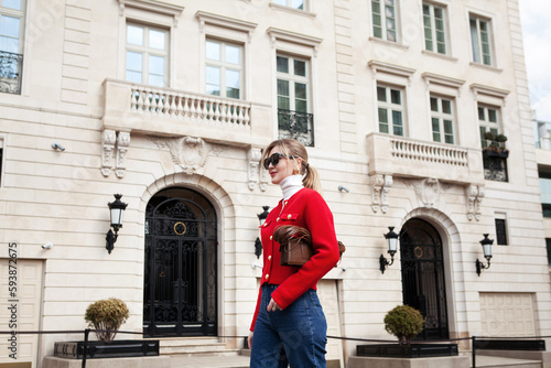 Outdoor portrait of young elegant fashionable woman wearing bright red jacket, leather bag, sunglasses, turtleneck walking in European city street. Trends of spring and summer © Anna Zhuk