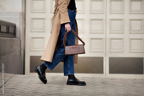 Side view woman walking street in fashionable spring or autumn clothes cashmere coat, jeans, black loafers shoes and handbag. Female model in motion, street style fashion, close up legs photo