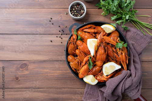 cooked crawfish in black saucepan with lemons and spices on wooden background
