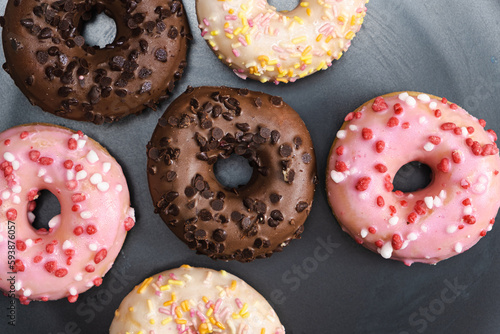 Lots of little donuts with white, pink and chocolate glaze on a black plate, top view