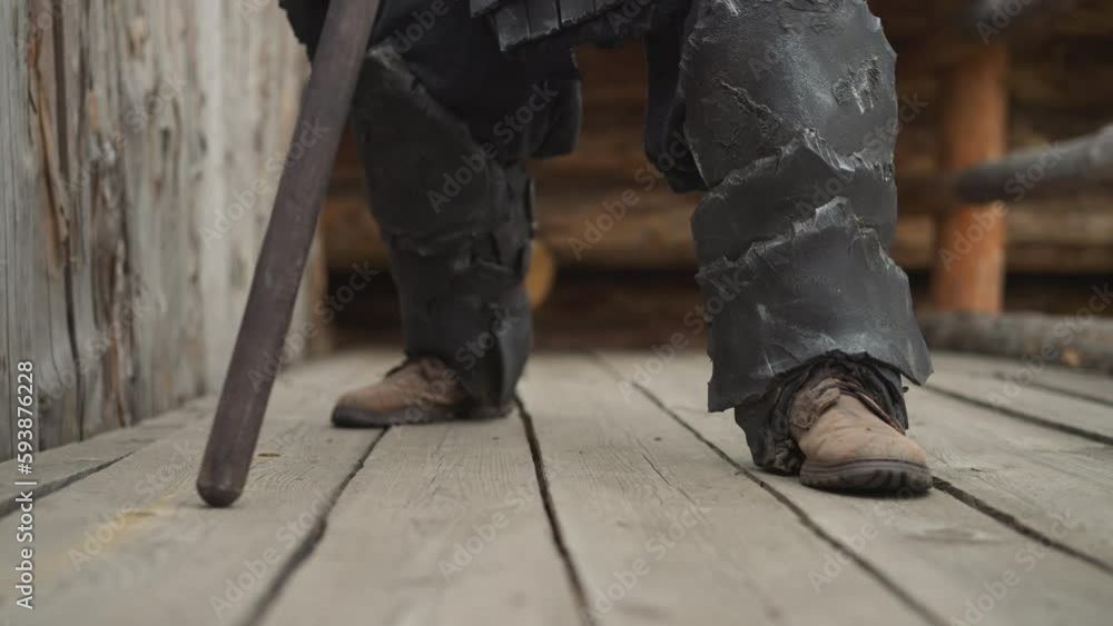 Knight walks on wooden bridge leaning on spear heavily. Strong medieval warrior prepares for duel in ancient village closeup on blurred background