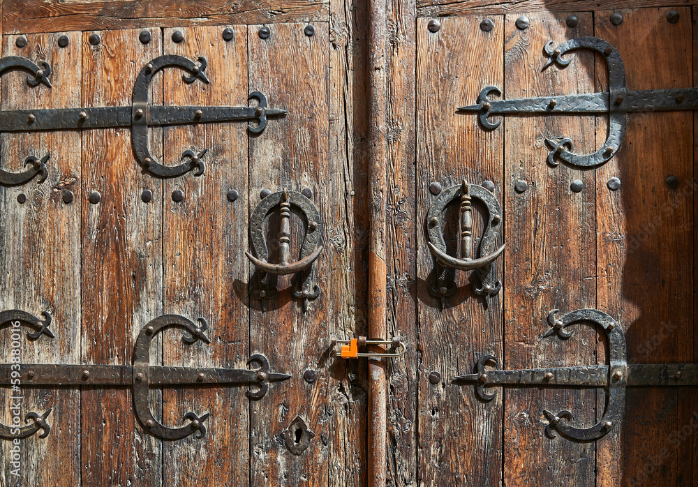 old wooden door with decorative wrought iron bolts and knockers and with a modern padlock old wooden door with decorative wrought iron bolts and knockers and with a modern padlock
