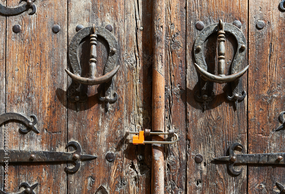 old wooden door with decorative wrought iron bolts and knockers and with a modern padlock