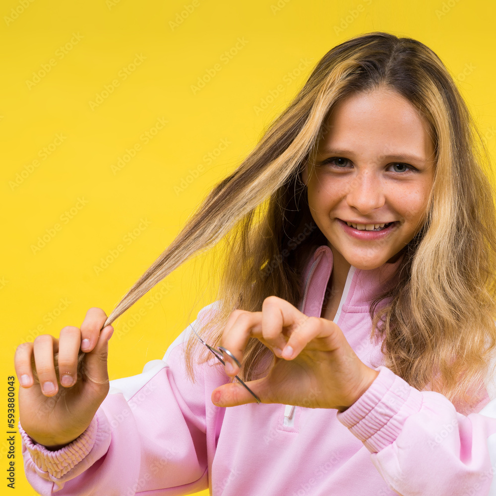 Child adorable girl hairdresser cutting long blonde hair with metallic scissors on yellow Child adorable girl hairdresser cutting long blonde hair with metallic scissors on yellow