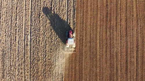 Tracteur dans un champ de terre avec une longue traînée de poussière. Tracteur vu du ciel passant le rouleau agricole. 