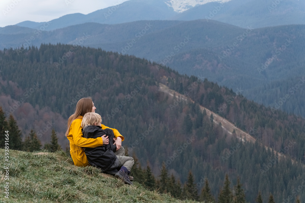 Mother and son rest and sit in an embrace on mountains background. Young mother with son sit on hillside