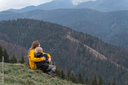 Mother and son rest and sit in an embrace on mountains background. Young mother with son sit on hillside