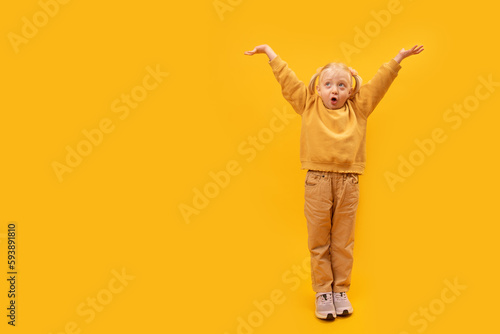 Wondered preschool girl in yellow clothes raised her hands up and seemed to holding something. Copy space, mock up