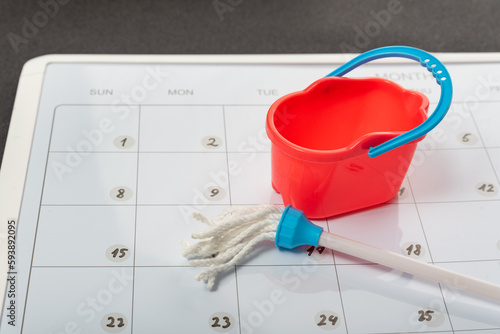 Toy bucket and mop on calendar background. Concept of spring general cleaning. Planned cleanup.