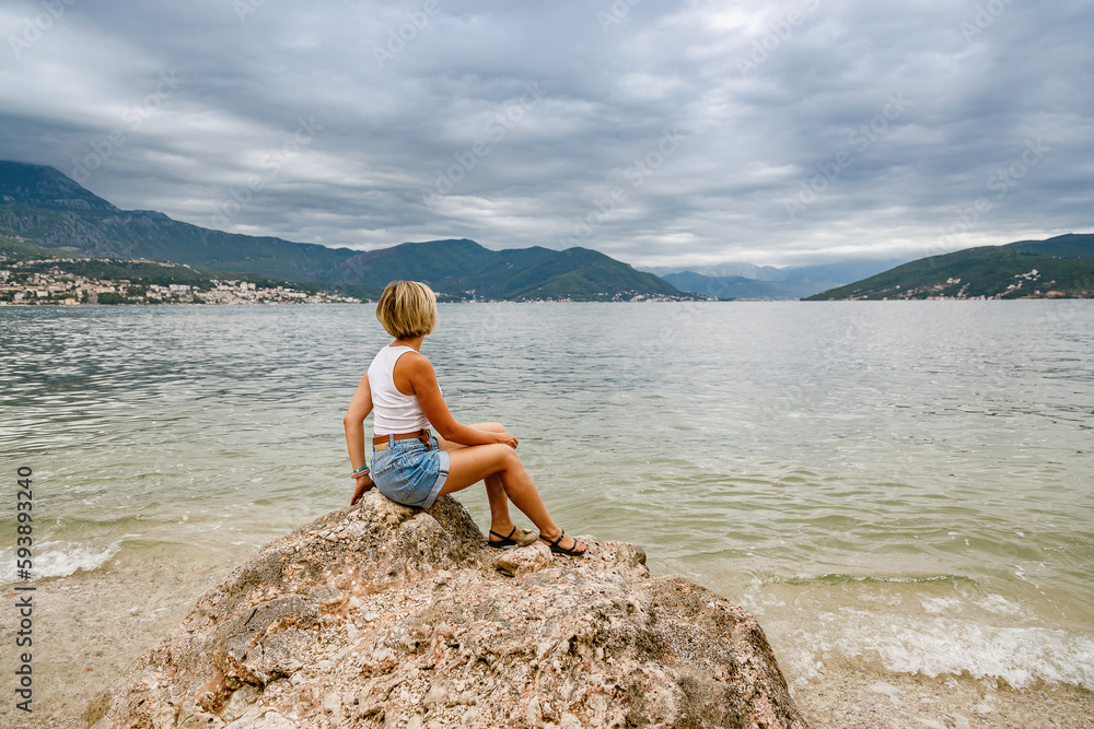 Woman sitting on a big stone, enjoying beautiful view of Boka-Kotor bay in Montenegro