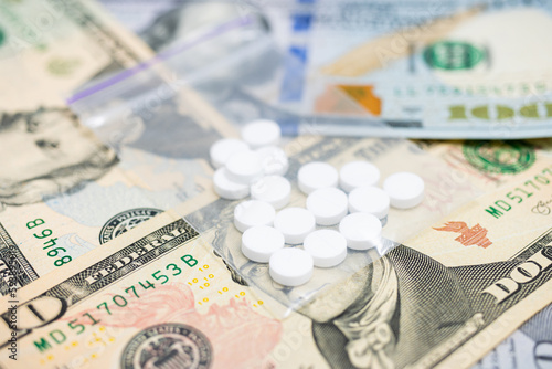 White round therapeutic pills for treatment or drugs in a transparent plastic bag with money, US dollar banknotes, expensive medicine and healthcare concept, close-up view