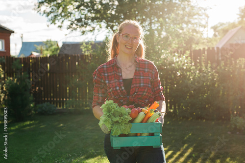 Female farmer carrying box of picked vegetables - garden and harvesting agricultural product for online selling. photo