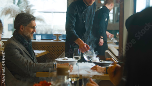 Couple on date in gastro cafe  drink wine and talk. Waiter and chef bring molecular dishes  pour liquid in meal for dish presentation with dry ice steam. Concept of molecular cuisine and public eating