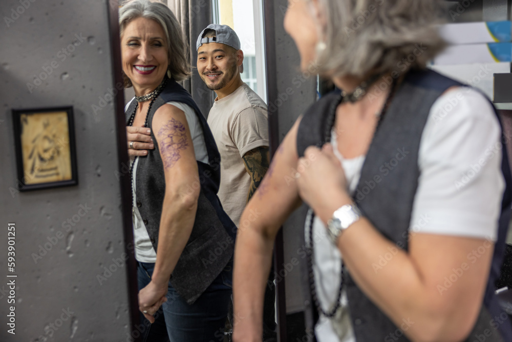 Fototapeta premium Long-haired woman looking in the mirror at her new tattoo
