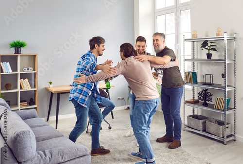 Male friends meet at a party at home, enjoy free time, drink beer, and have fun together. Group of young and mature men hugging in the living room. Friendship and leisure concept