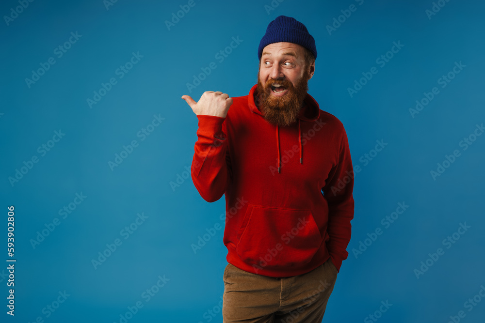 Naklejka premium Excited man pointing finger away at copy space isolated over blue background