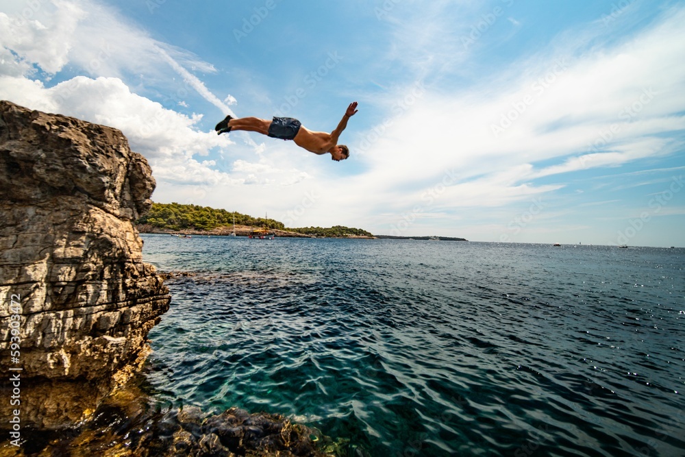 Fototapeta premium Guy jumping into the sea with a cloudy blue sky in the background in Croatia