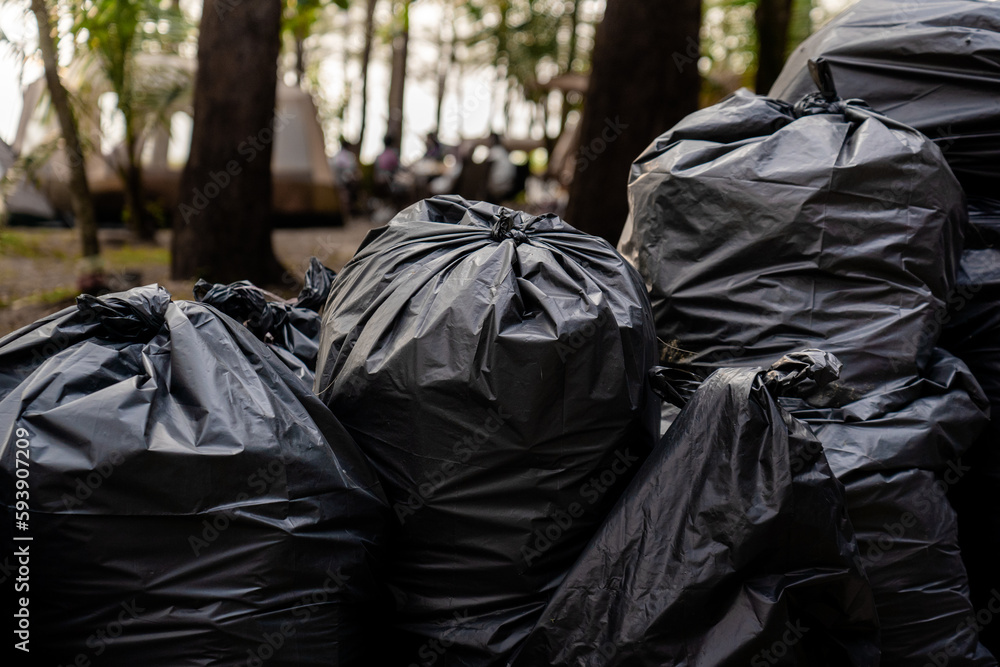 pile of disposable black garbage bags placed on ground around camping area full of trash separated wet waste and plastic for recycling, volunteer cleaning beach for protecting the environment