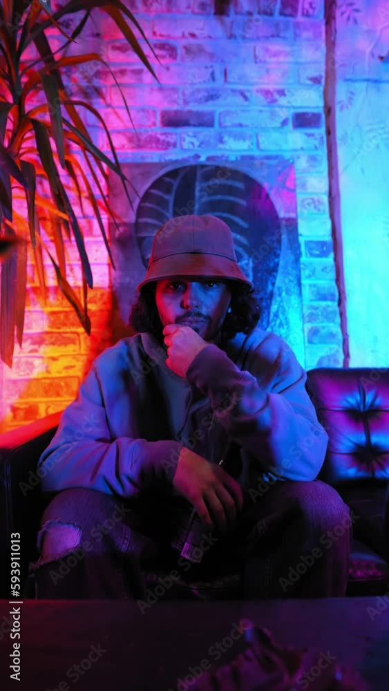 Vertical Video, Portrait of a Handsome Bearded Man in a Panama Hat in Neon Lighting. Stylish Cool Guy Looking at the Camera. Slow Motion. Vertical Video, Portrait of a Handsome Bearded Man in a Panama Hat in Neon Lighting. Stylish Cool Guy Looking at the Camera. Slow Motion.