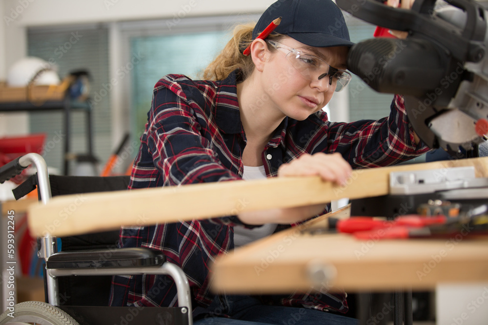 female carpenter in wheelchair lowering blade on circular saw female carpenter in wheelchair lowering blade on circular saw
