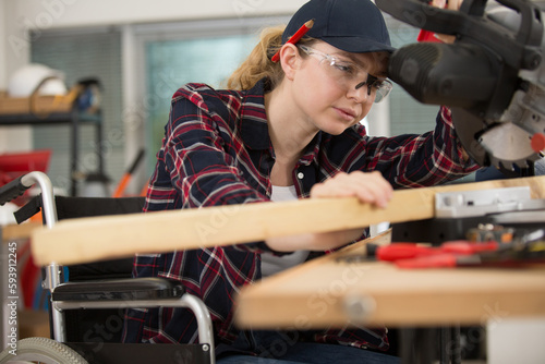 female carpenter in wheelchair lowering blade on circular saw