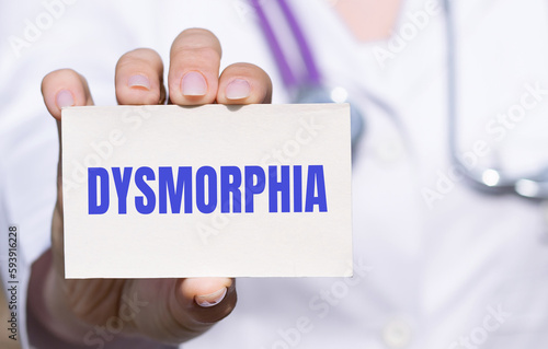 Dysmorphia - word on card in doctors hand, body dysmorphic disorder concept, gray background photo