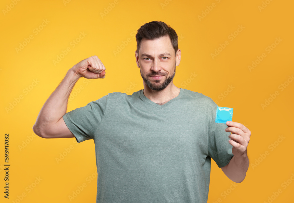 Handsome man holding condom on orange background Handsome man holding condom on orange background