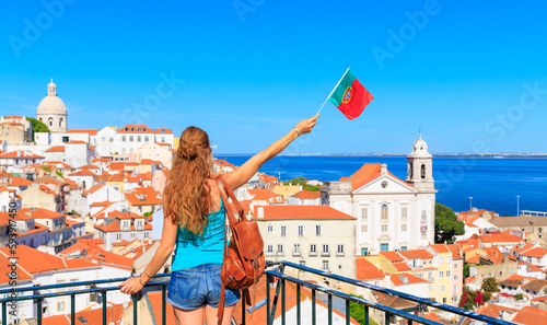 Woman with arms raised holding portuguese flag looking at viewpoint of Lisbon